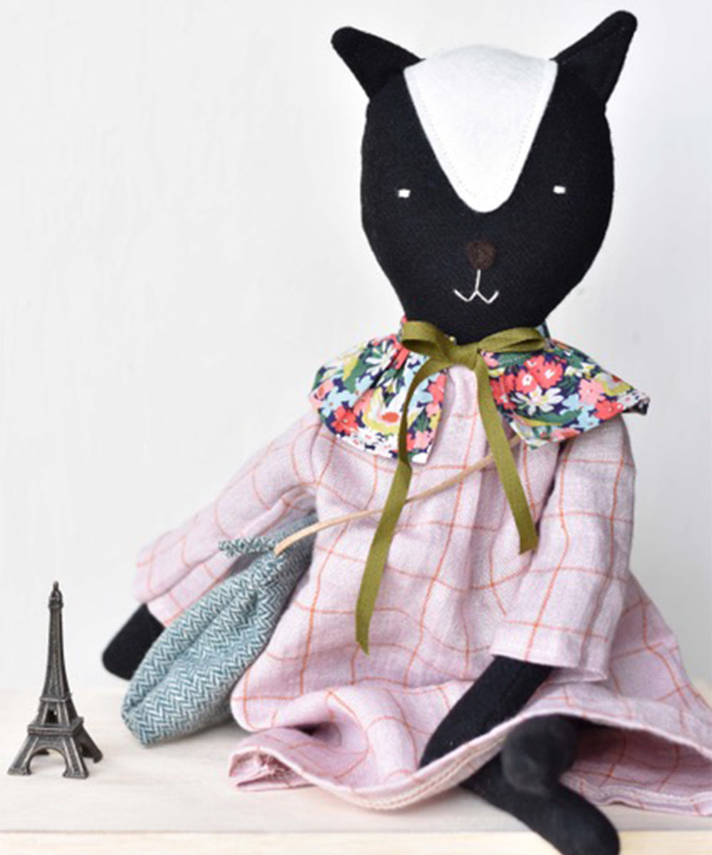 Scout le Skunk, a black-and-white cat doll in a dress, sits beside a small Eiffel Tower figurine.