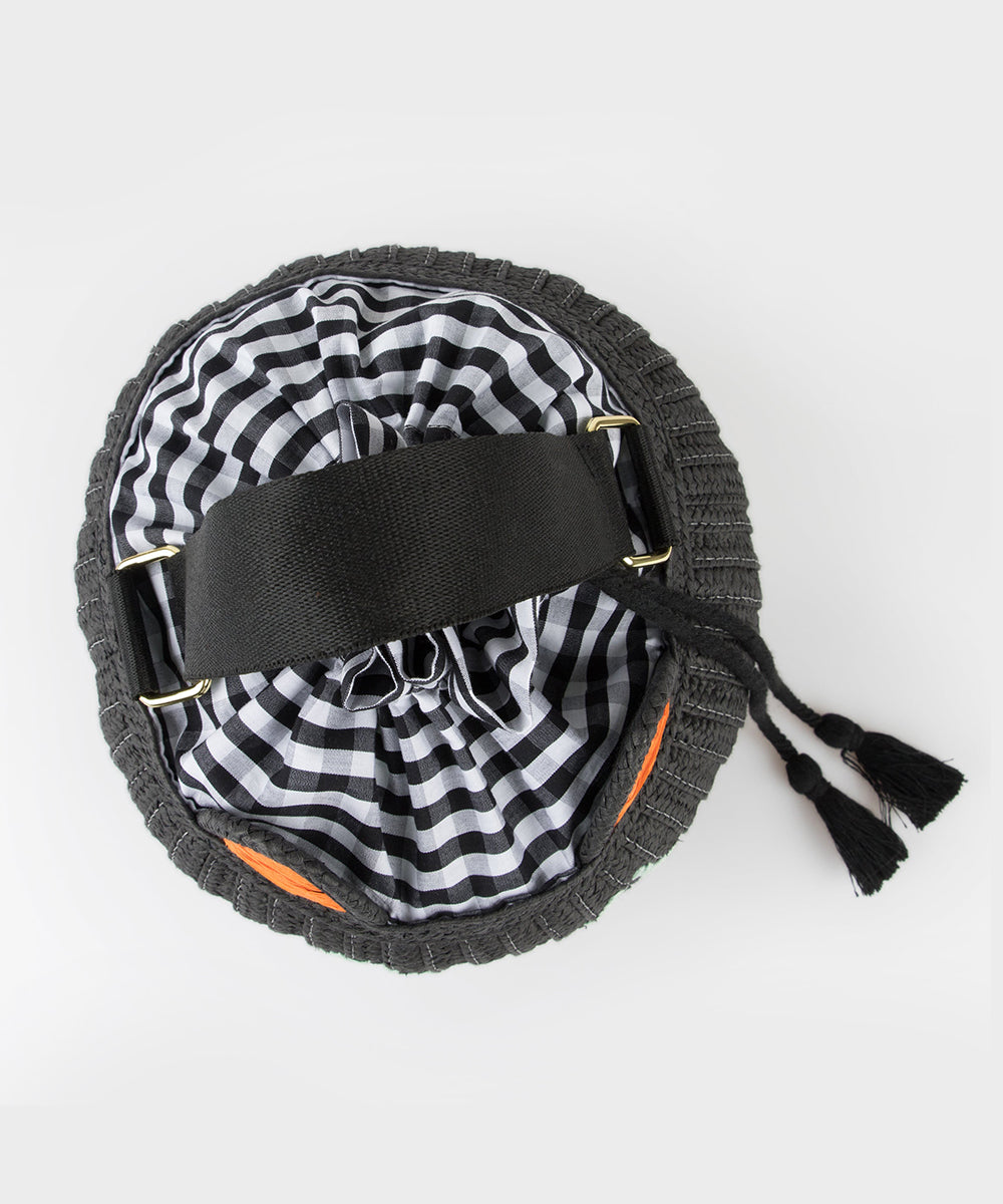 Top view of the Le Cat Basket Bag, a round black bag featuring a black-and-white checkered lining and black tassel drawstrings.