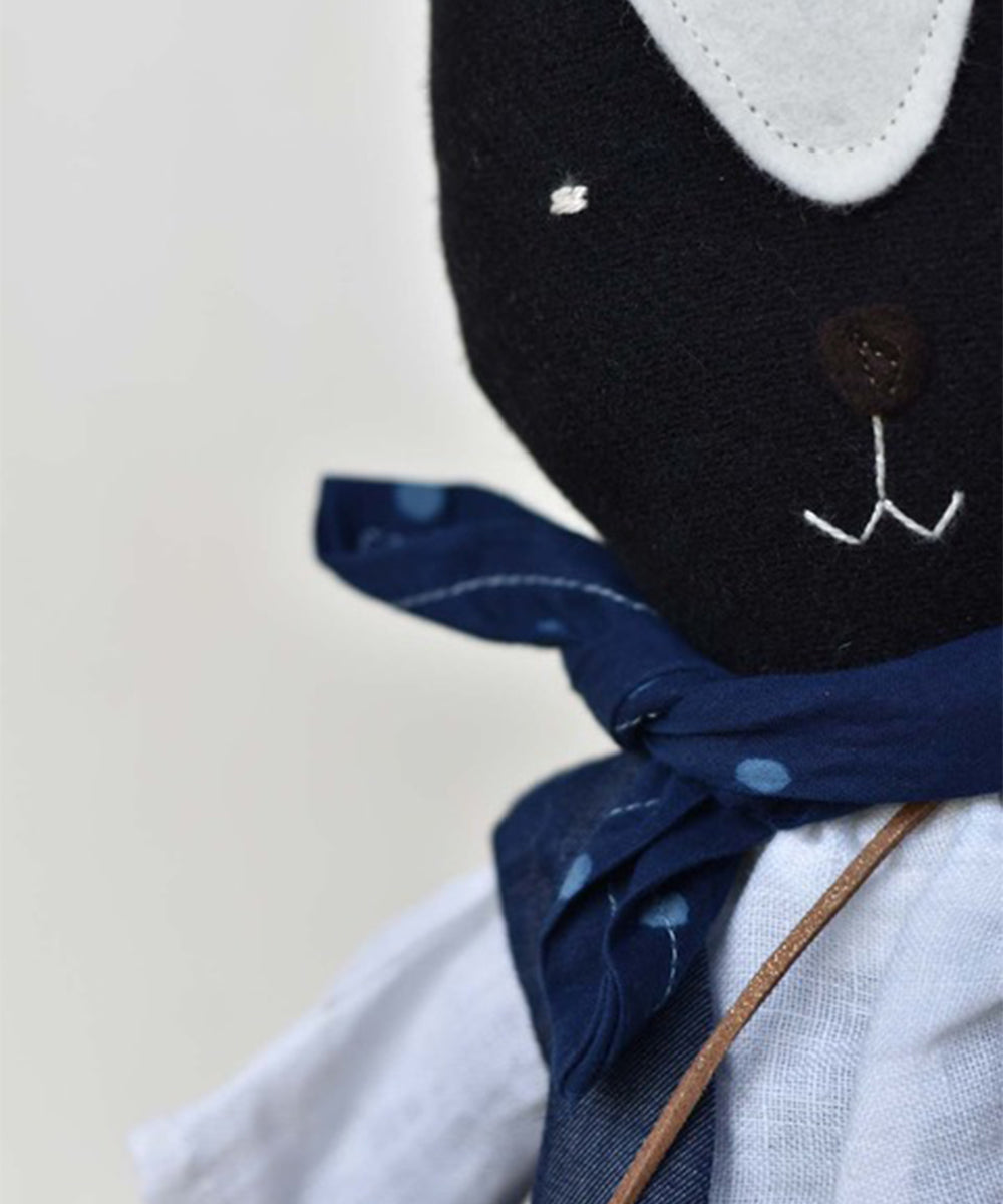 Close-up of Theo le Skunk, a black fabric animal toy wearing a blue scarf with white polka dots and a white shirt.