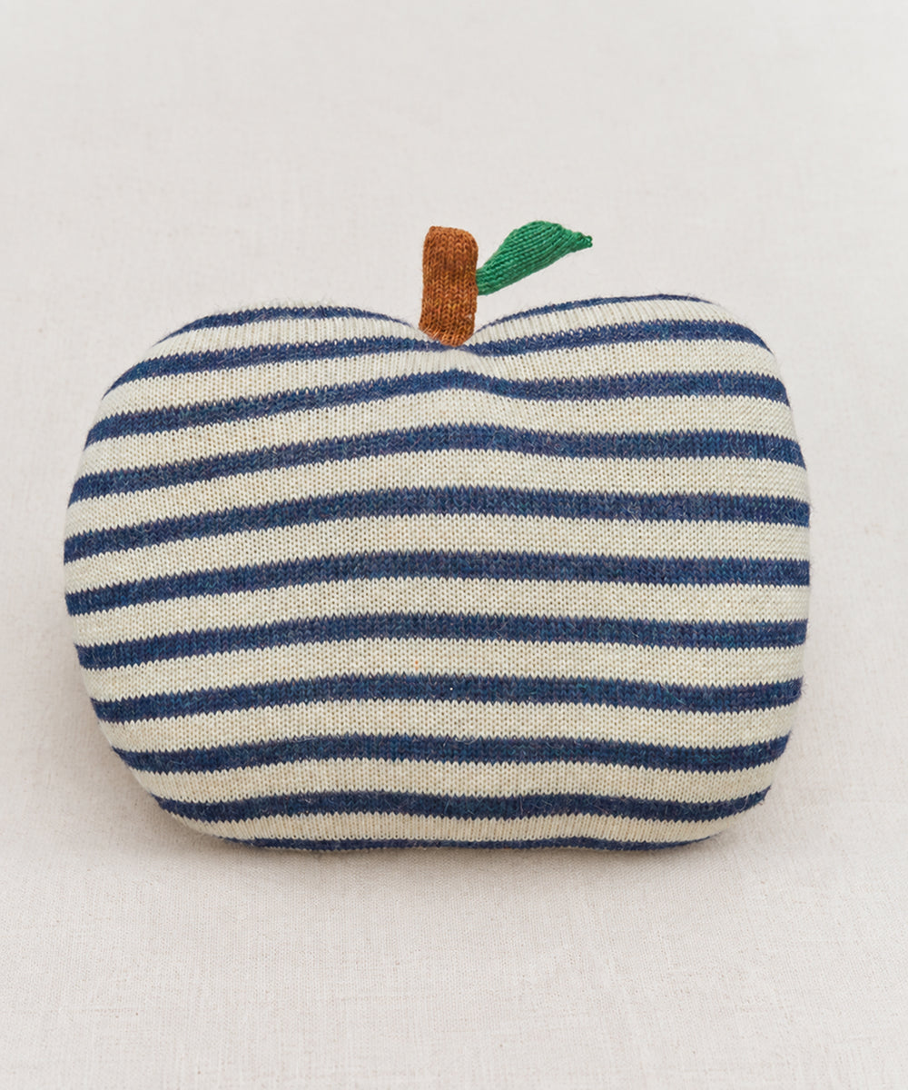 An Apple Pillow with blue and white stripes, brown stem, and green leaf sits on a light fabric surface.