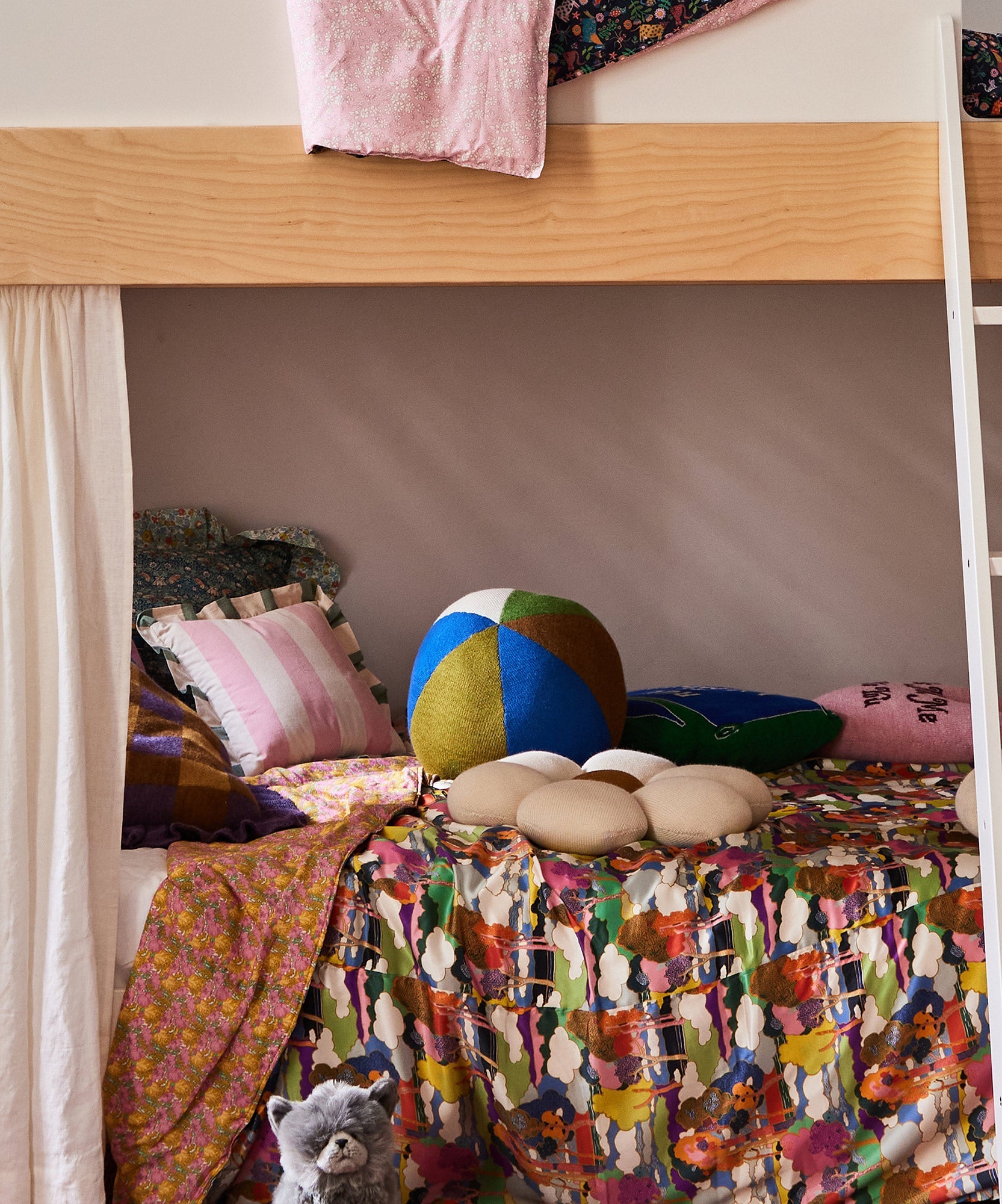Colorful, patterned bunk bed with pillows, a plush cat toy in the corner, and a Circus Ball - Royal Blue at the bottom.