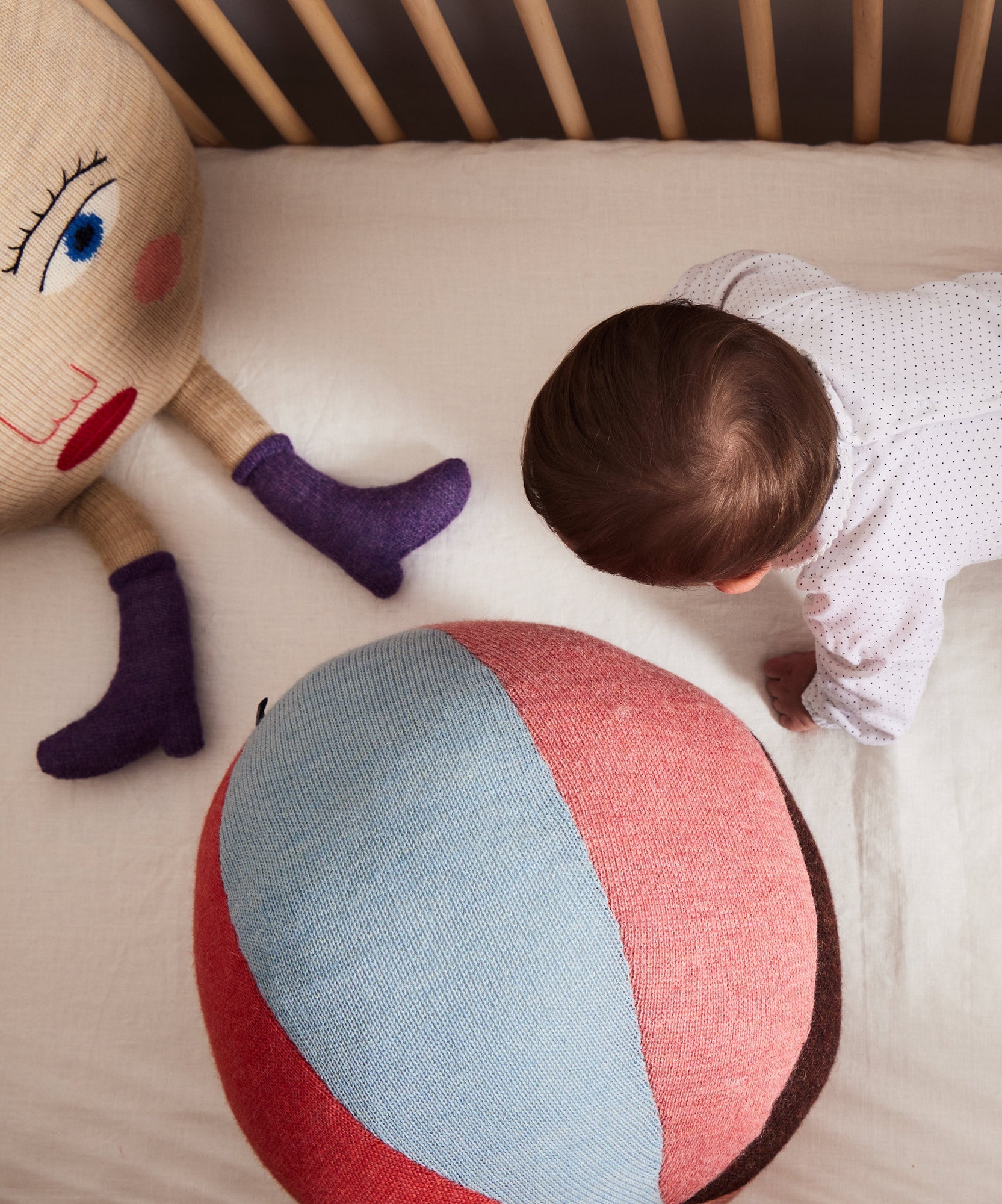 Baby crawling on a white sheet near the Circus Ball - Rose and a doll with a face, purple boots, and blue eye.