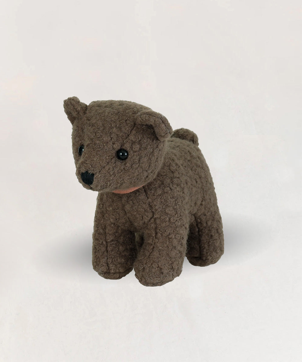 Eustache le Bear, a small brown plush toy, stands on a plain, light-colored surface.