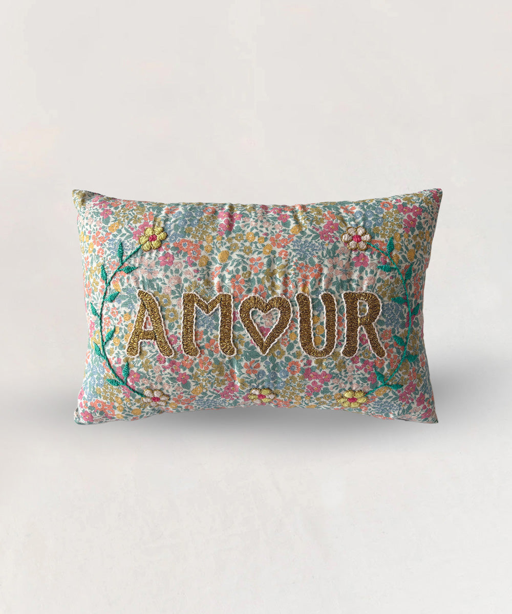 Le Mini Embroidered Pillow - Floral Amour: rectangular pillow with "AMOUR" embroidered on a vibrant floral-patterned fabric.