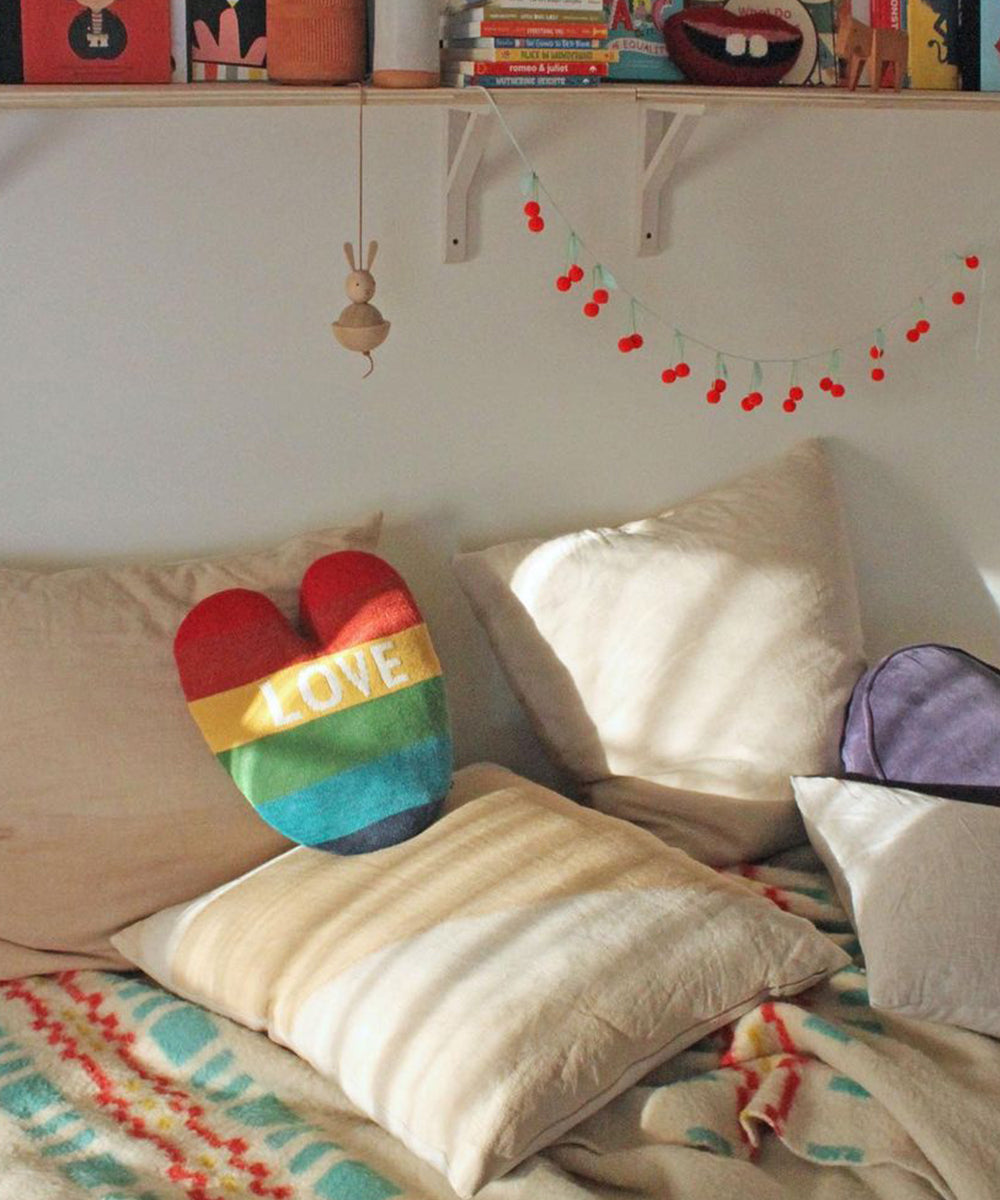 Cozy bed with Heart Pillow - Rainbow, cream bedding, and cherry garland hanging above.