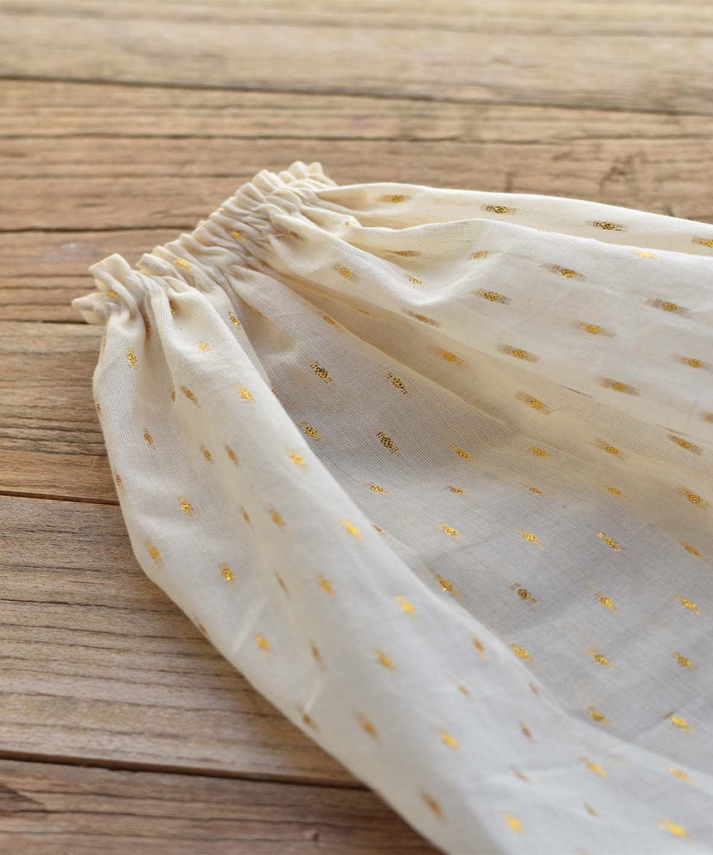 Close-up of the Mae le Cat – Field Skirt’s cream fabric sleeve with gold dots and an elastic gathered cuff, shown on a wooden surface.