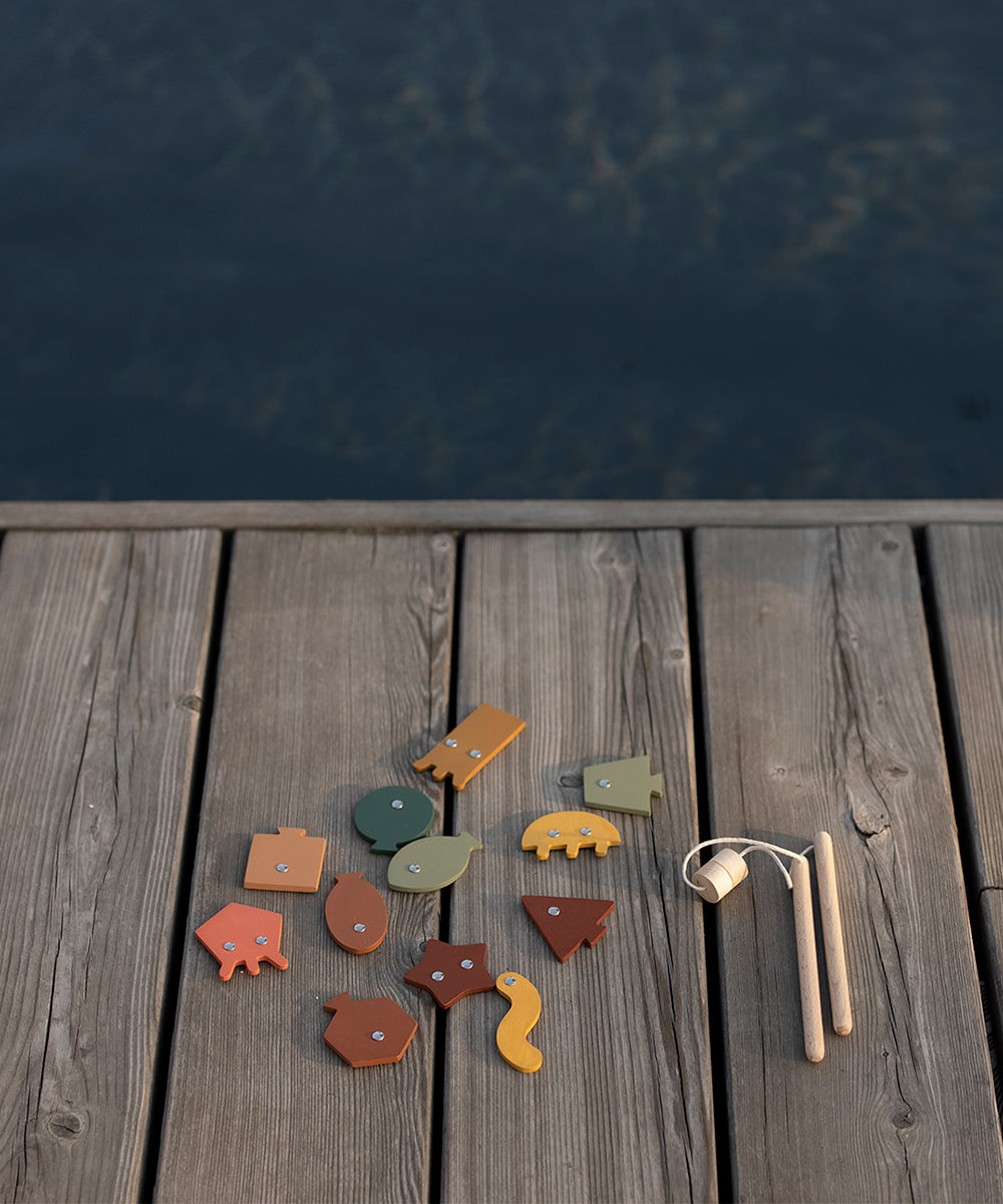 The Wooden Fishing Game features animal shapes on a dock by the water, with a toy fishing rod placed on the right side.