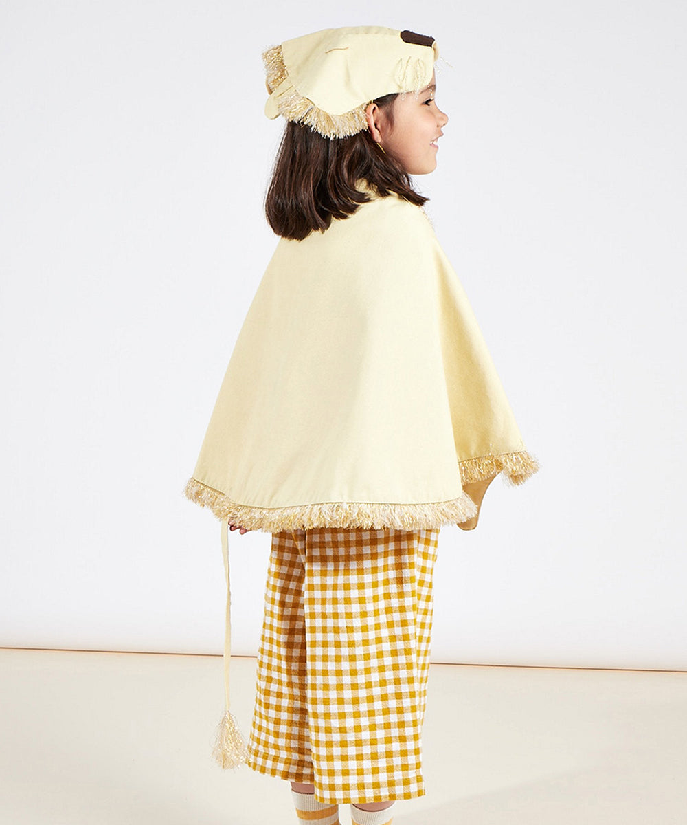 Young girl wearing the Lion Costume: a yellow cape, matching hat with fringe, and yellow checkered pants, standing sideways.