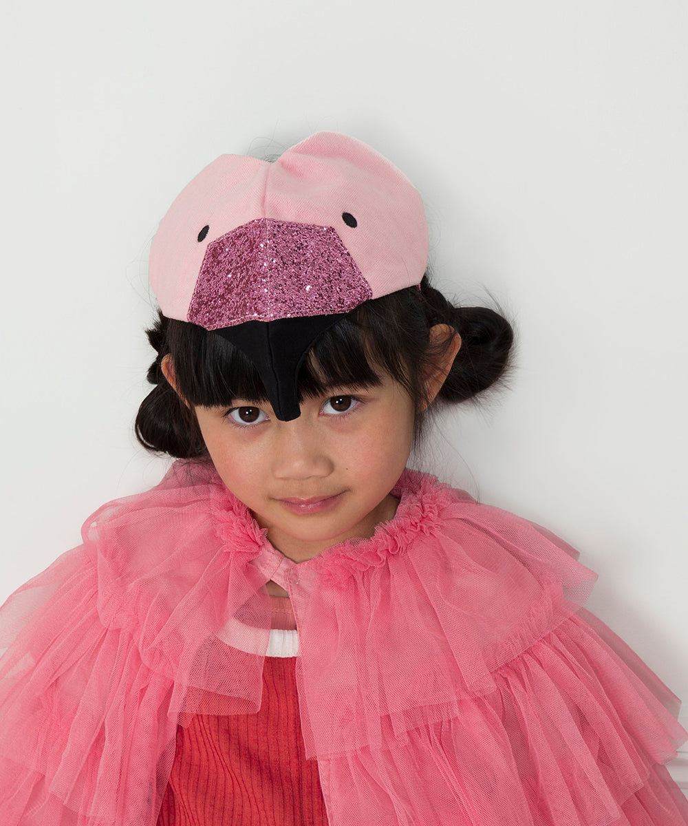 Young girl wearing the Flamingo Costume, featuring a pink flamingo hat and ruffled pink cape, looking at the camera with a slight smile.