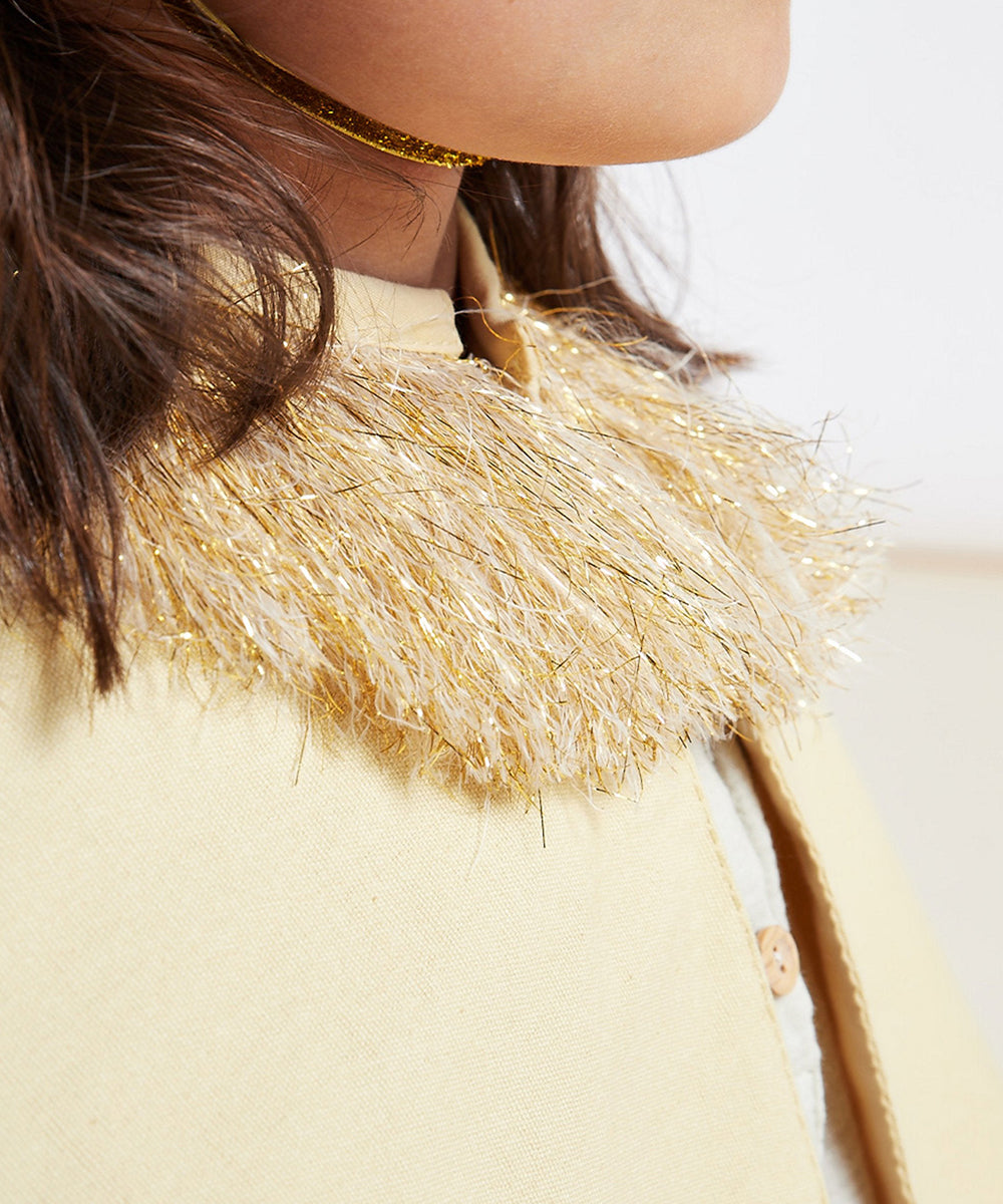 A child in a Lion Costume featuring a gold and cream tinsel collar and light yellow cape, shown from the side.