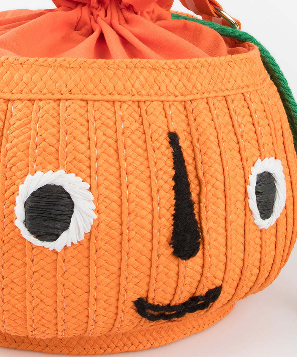 Le Pumpkin Basket Bag is a woven orange pumpkin-shaped bag featuring a smiling face with black and white eyes.