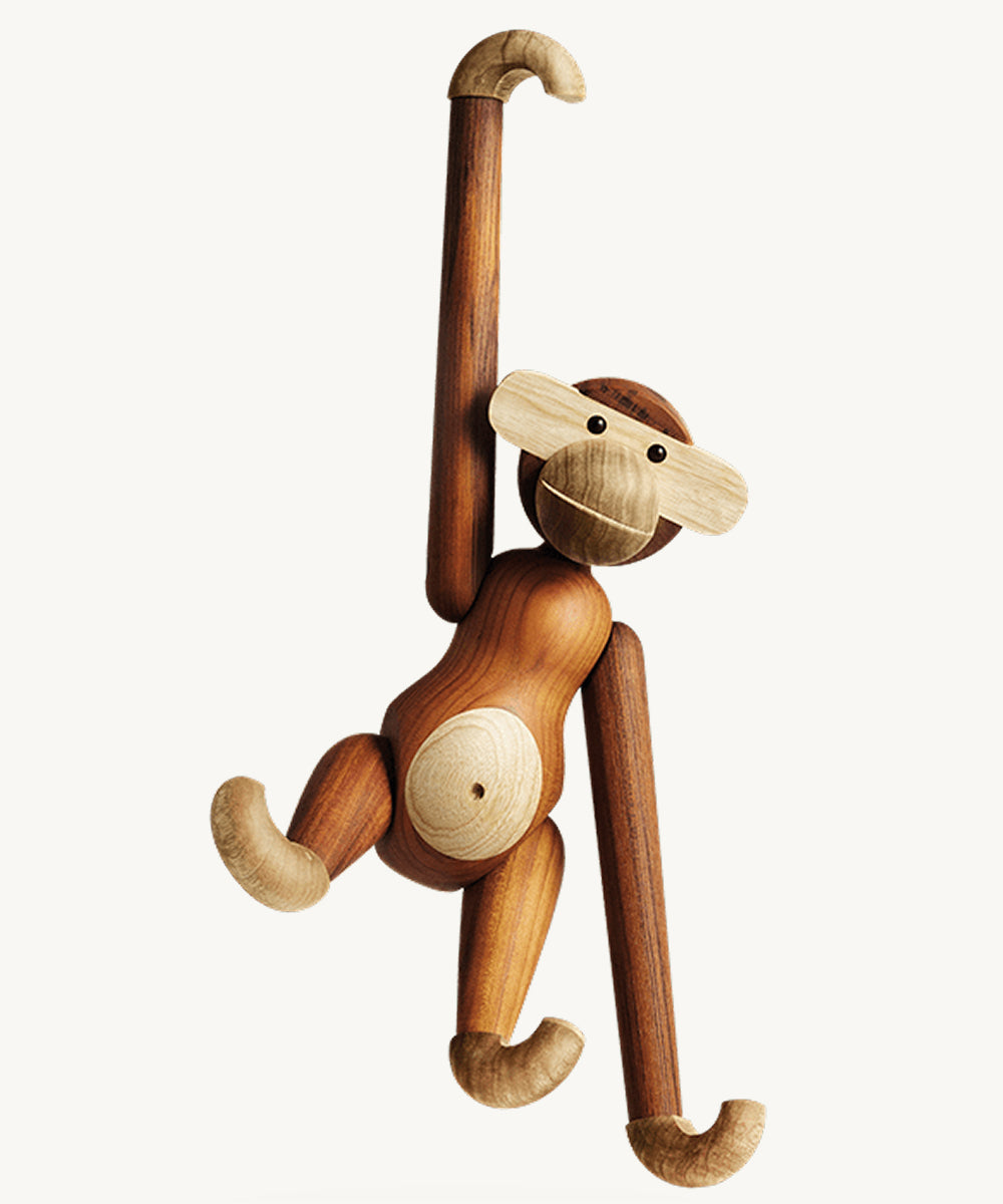 Le Monkey by Kay Bojesen is a wooden monkey toy with jointed limbs and two-tone wood details on its face, belly, hands, feet, hanging by one curved arm.