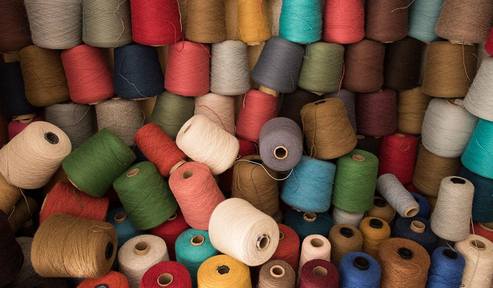 Stacks of colorful yarn spools in various shades, including red, green, blue, and beige, arranged closely together.