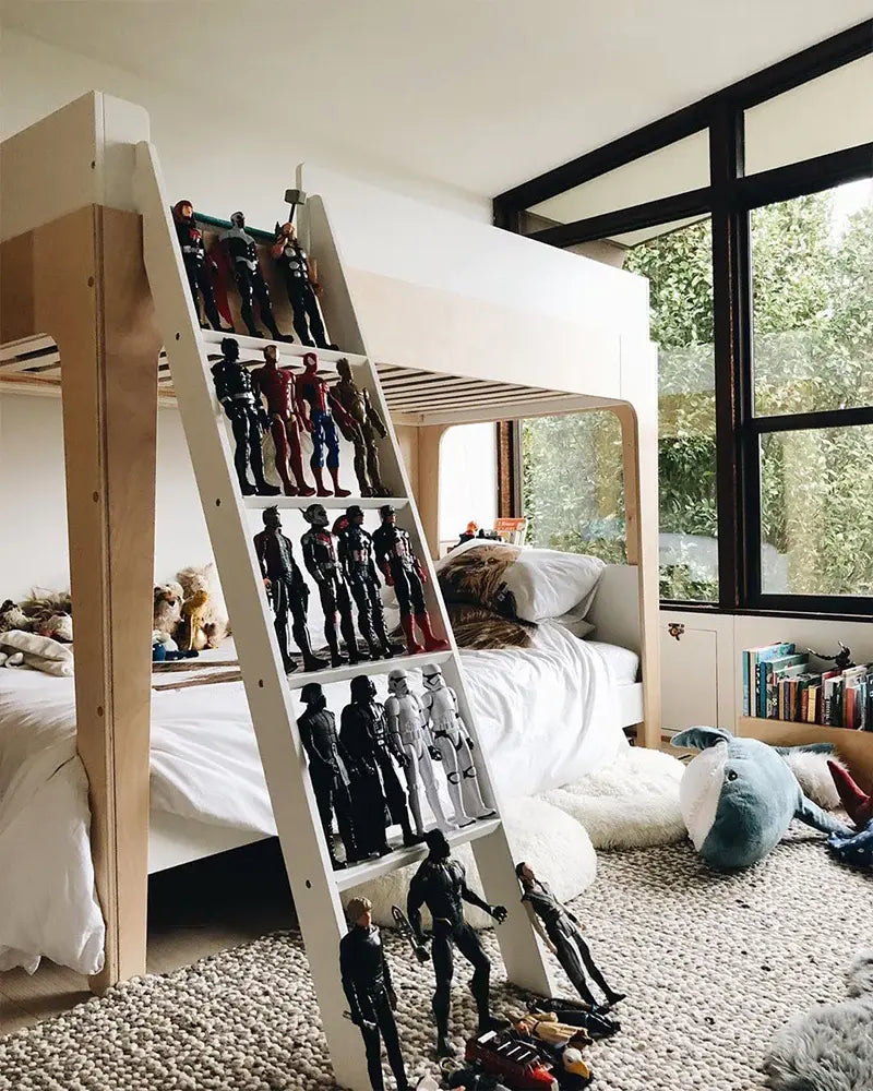 A bunk bed ladder lined with action figures in a childs room. The room has stuffed animals, a rug, and a bookshelf, with natural light coming through large windows.