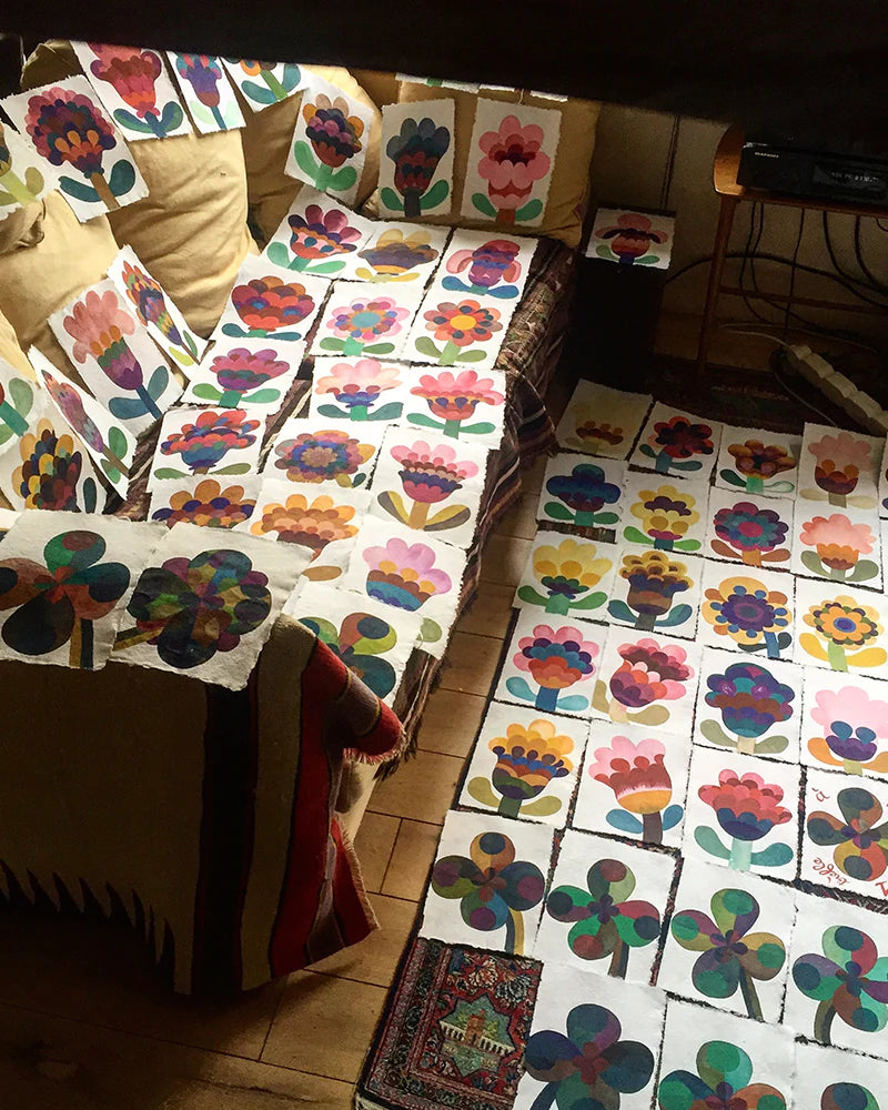 A room with a couch and floor covered in colorful flower paintings on canvases. The paintings feature various floral designs and patterns.