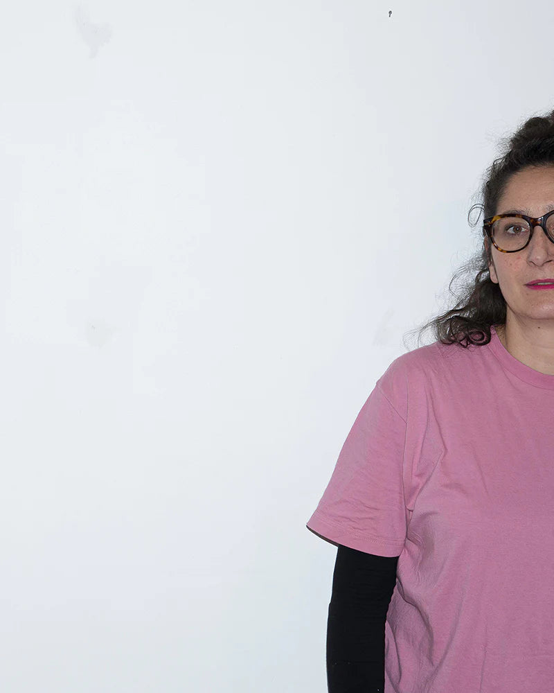 Person wearing glasses and a pink T-shirt stands against a plain white background, partially out of frame.