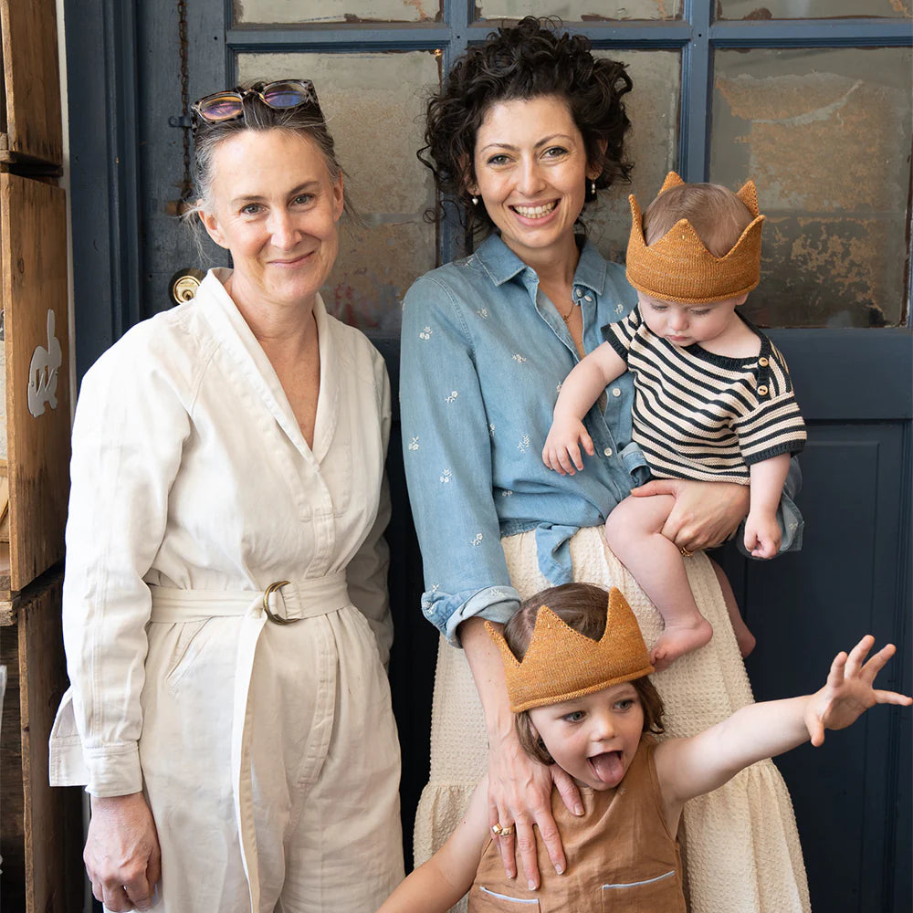 Two adults and two children wearing crowns are posing for a photo indoors. One adult is holding a baby.