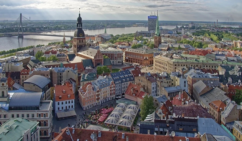 Aerial view of an old city with historic buildings, a river, and a bridge in the background. A prominent cathedral tower rises above the surrounding architecture.