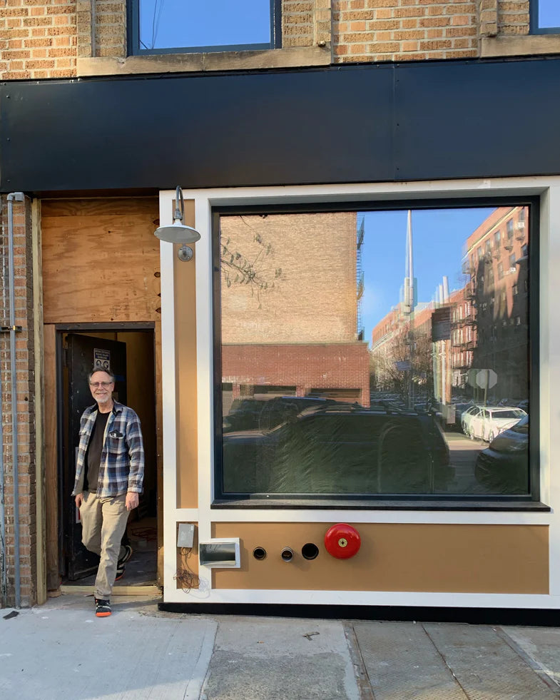 A man in a plaid shirt and glasses stands in the doorway of a building with a facade resembling a vintage camera, featuring a large window as the lens.