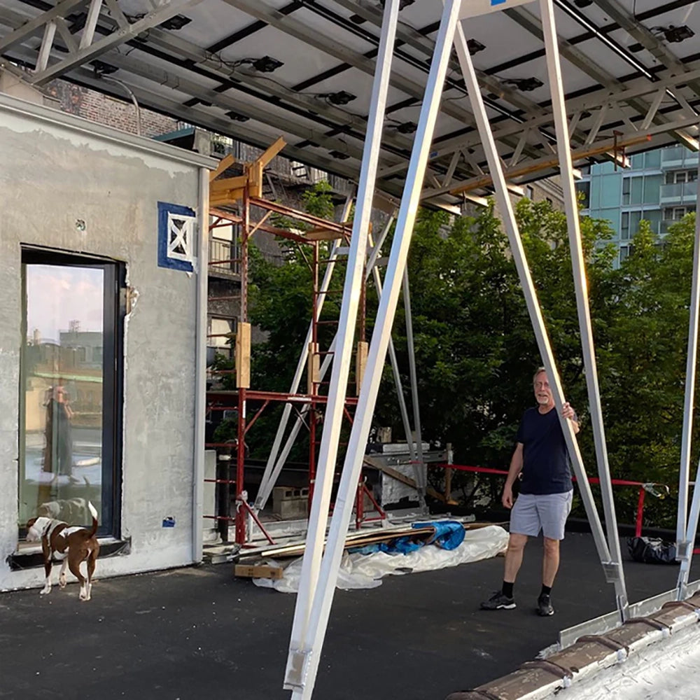 Man standing on a rooftop with a dog nearby, surrounded by scaffolding and construction materials. A glass door reflects the scene.