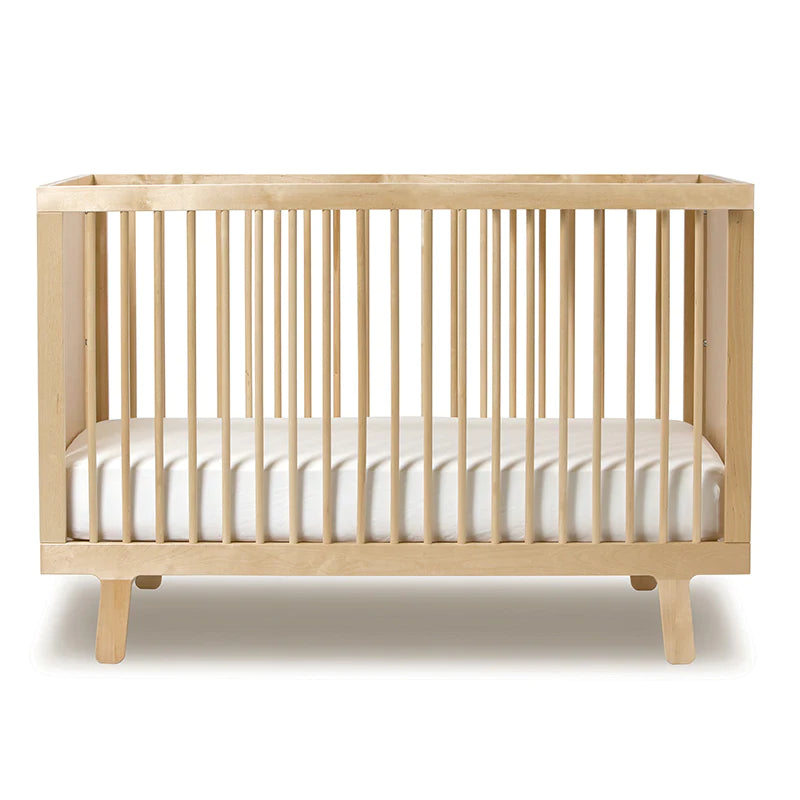 Wooden baby crib with vertical slats and a white mattress, placed on a white background.