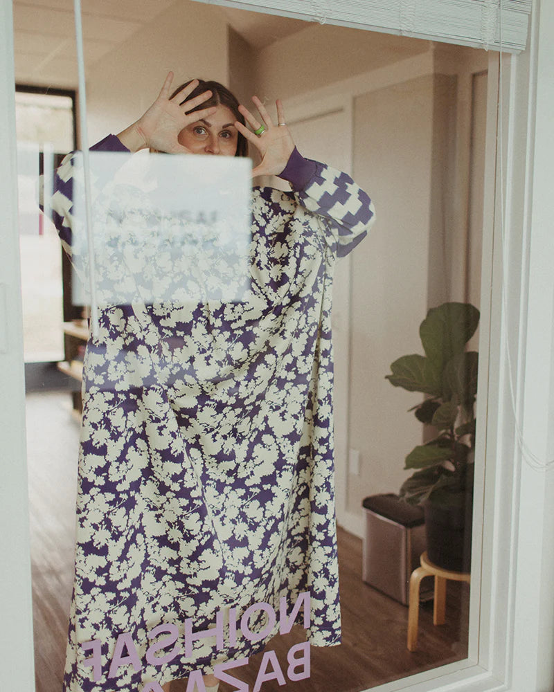 Person in a floral dress poses playfully with hands splayed on a glass door.