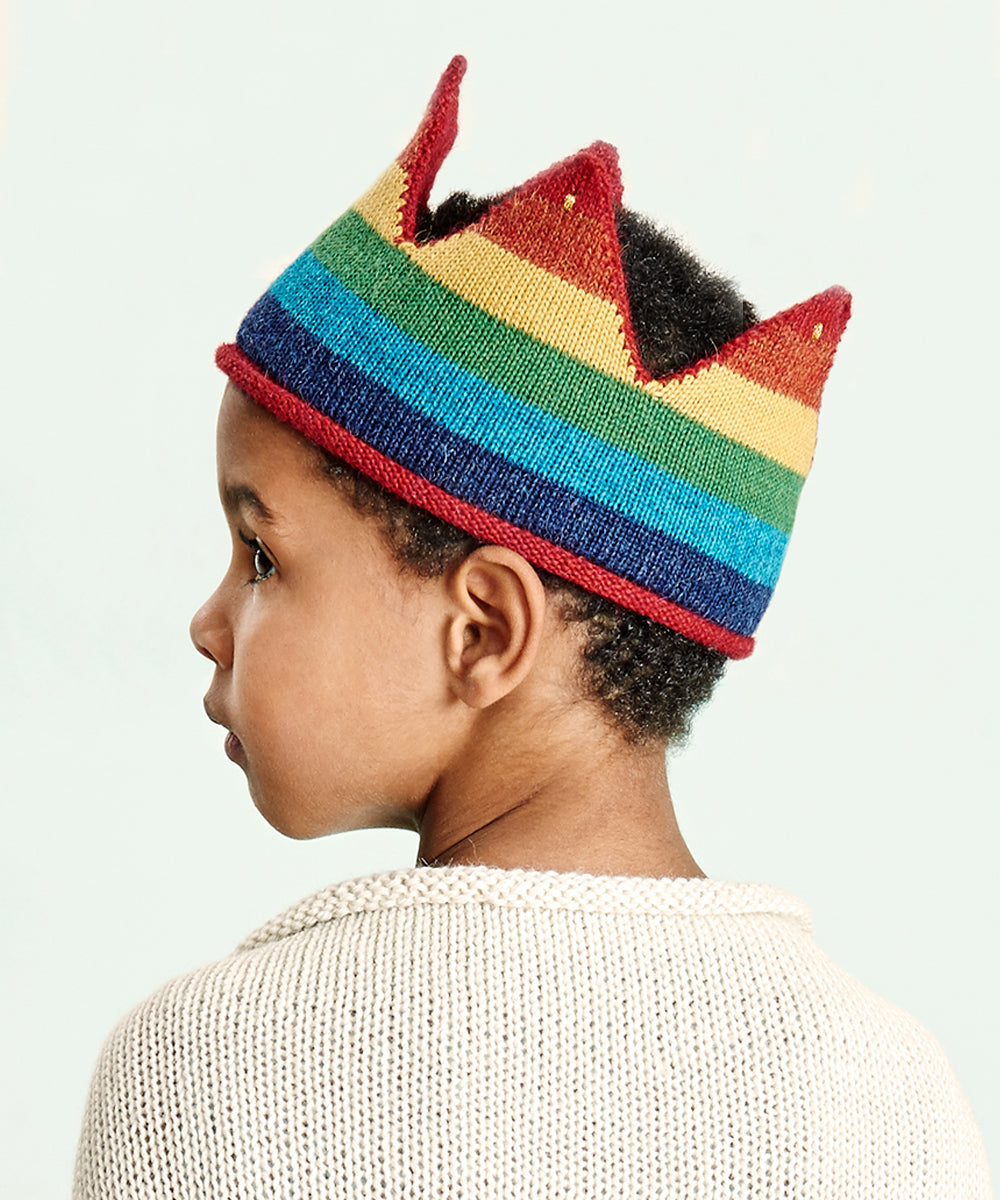A young child in a cream sweater wears the Rainbow Crown, looking left against a light background.