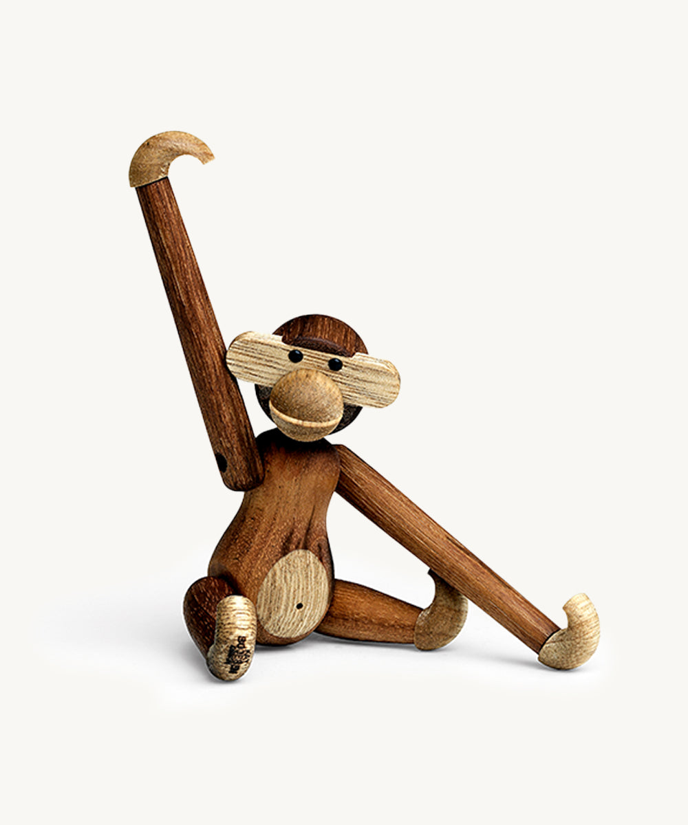 Le Monkey by Kay Bojesen, a wooden toy monkey with one arm raised and one leg extended, sits on a white background.