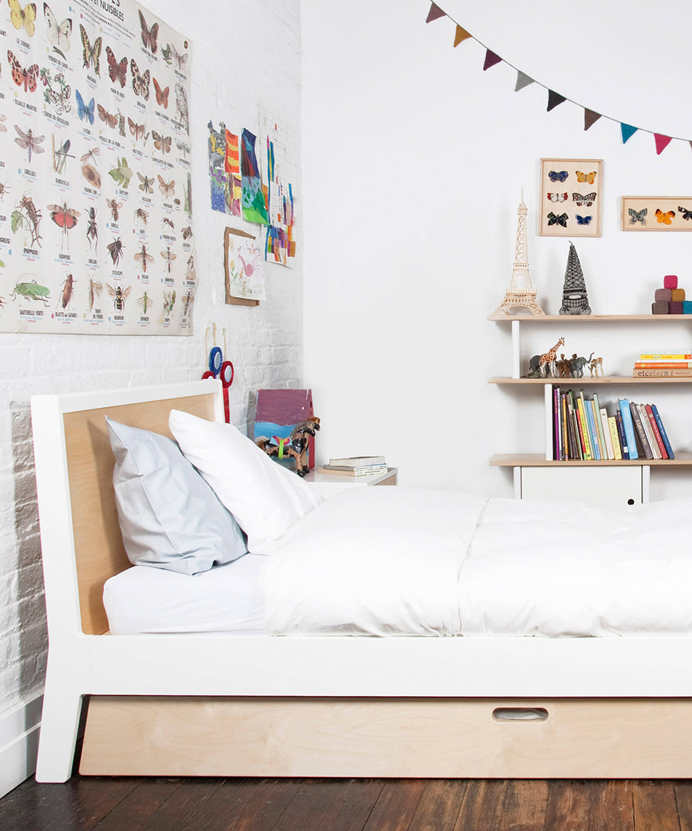A neatly made Sparrow Twin Bed and Trundle Bed in a child's room surrounded by books, toys, butterfly posters, and colorful bunting on the walls.