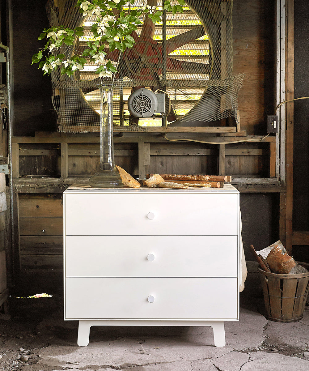 Sparrow 3-Drawer Dresser topped with a vase holding branches, set in a rustic wooden room with a fan.