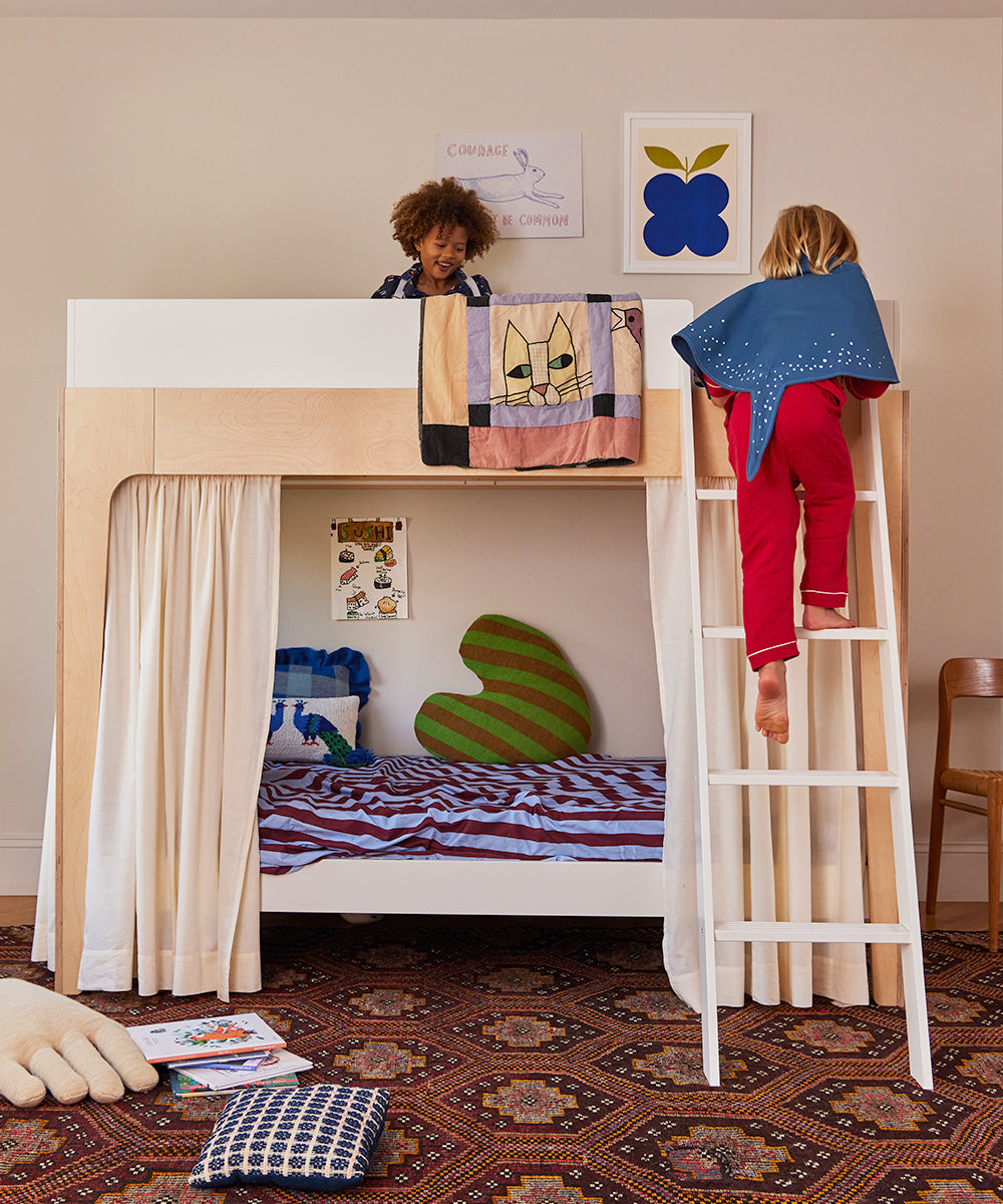 Two children wear Le Stingray Costume Wings; one climbs a ladder while the other smiles on the top bunk.