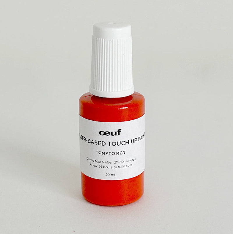 A small, red bottle labeled Touch-up Paint: Tomato Red sits on a light surface.