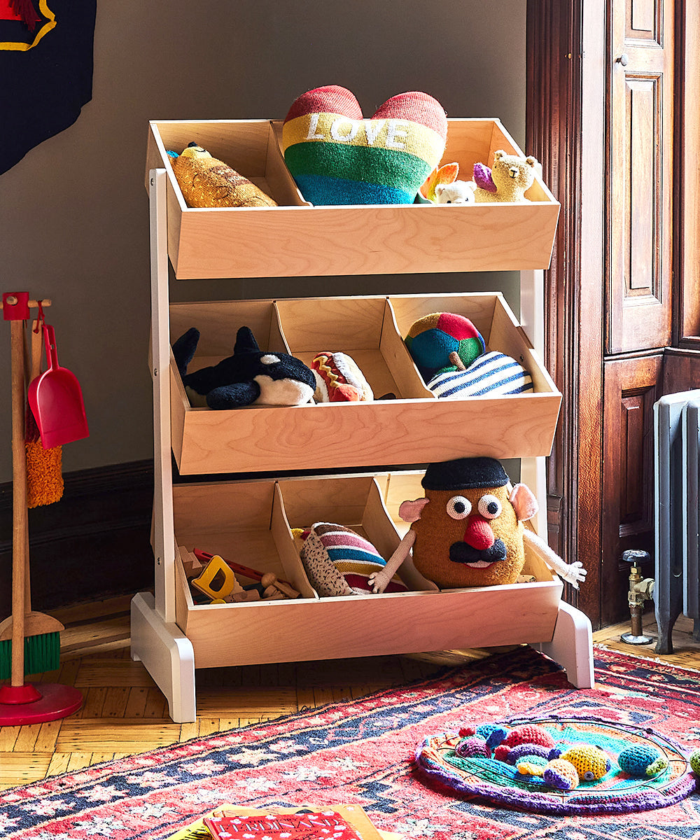 Heart Pillow - Rainbow sits among plush toys in a cozy, sunlit room, displayed on a three-tier wooden toy organizer.
