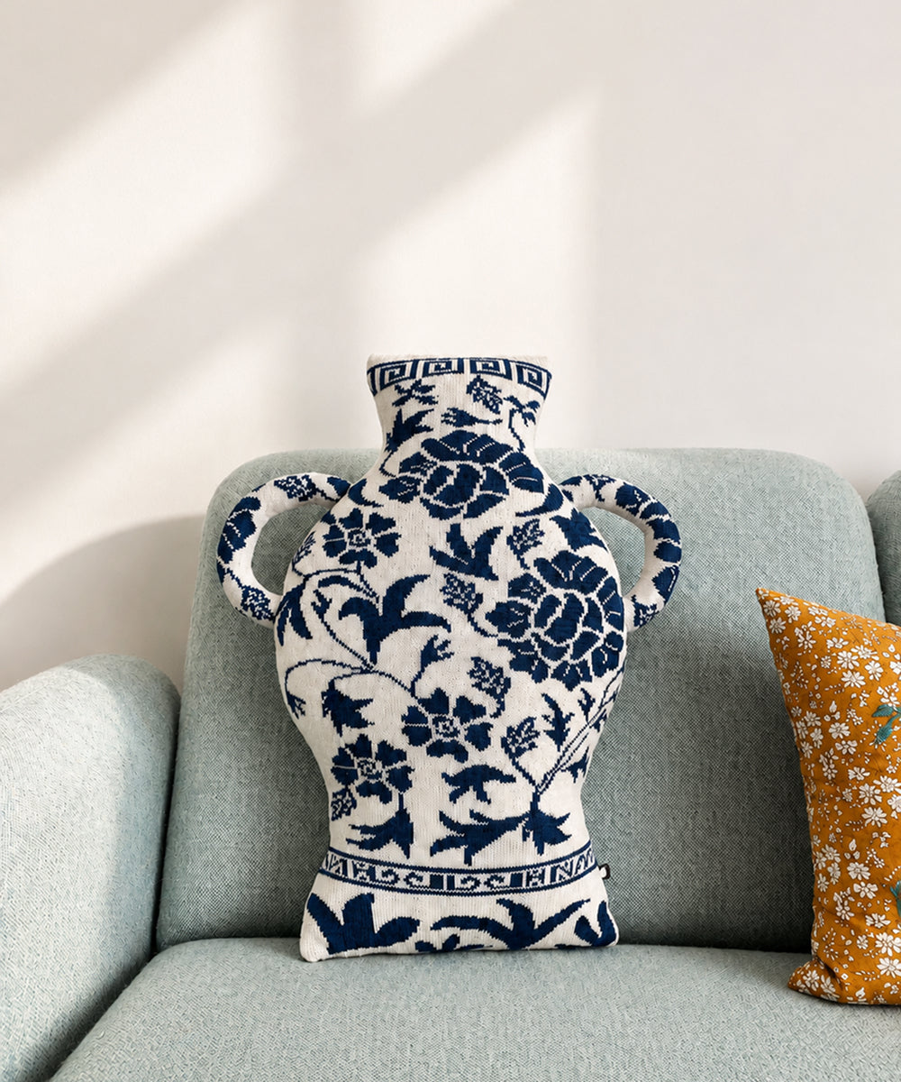 The Porcelain Vase Pillow, featuring blue and white floral designs, rests on a light gray couch beside a yellow patterned cushion.
