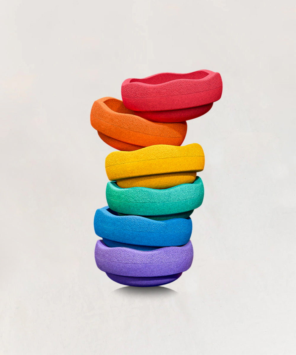 The Le Original Rainbow features six colorful, textured rings stacked in a wavy tower and arranged in rainbow order on a plain background.
