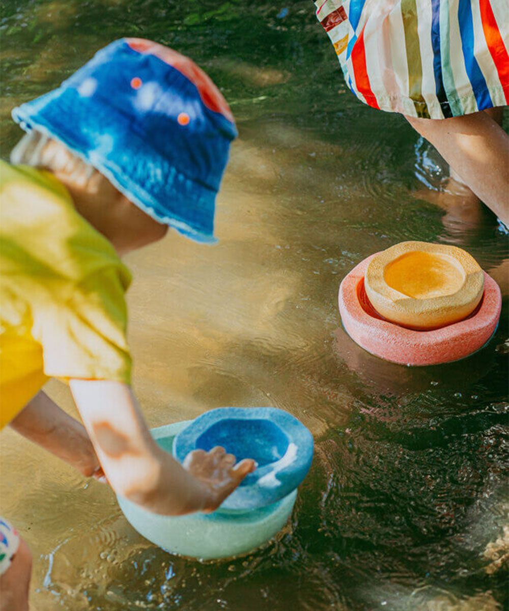 Two children play outdoors in shallow water with Le Inside Rainbow colorful stacking bowls.