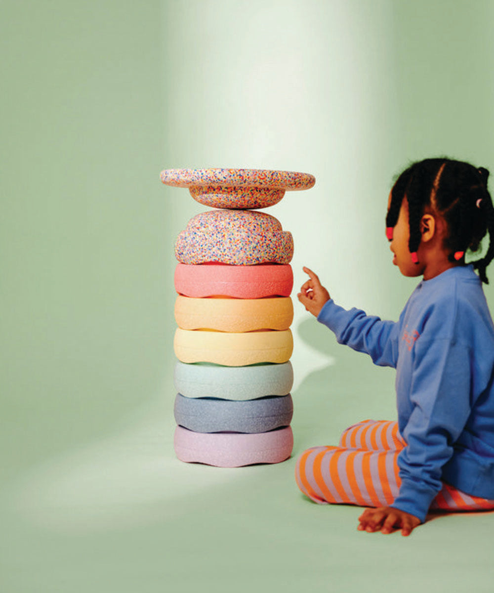 A child points at a tall stack of Complete Set cushions, colorful and round, against a pale green background.