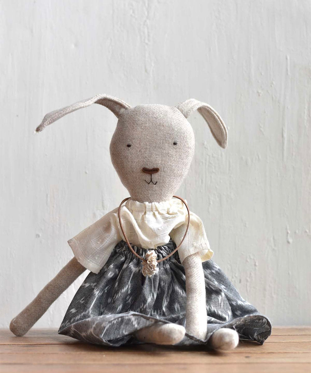 Ruthie le Rabbit - Ikat Skirt: stuffed bunny doll in a white top, gray patterned skirt, and necklace, sitting on a wooden surface.