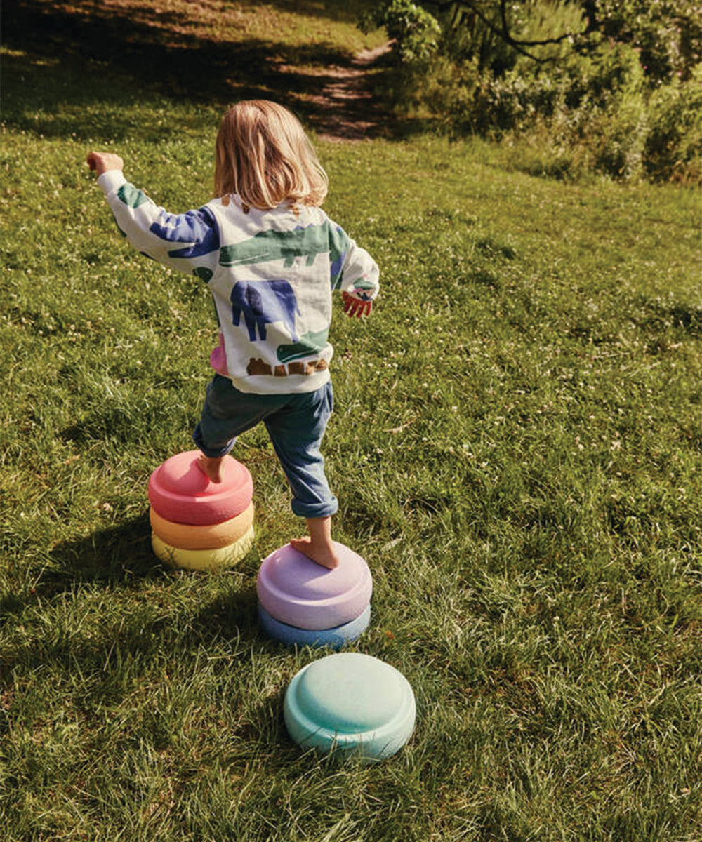A child balances on the Complete Set stepping stones outdoors on grass, wearing a patterned sweatshirt and jeans.