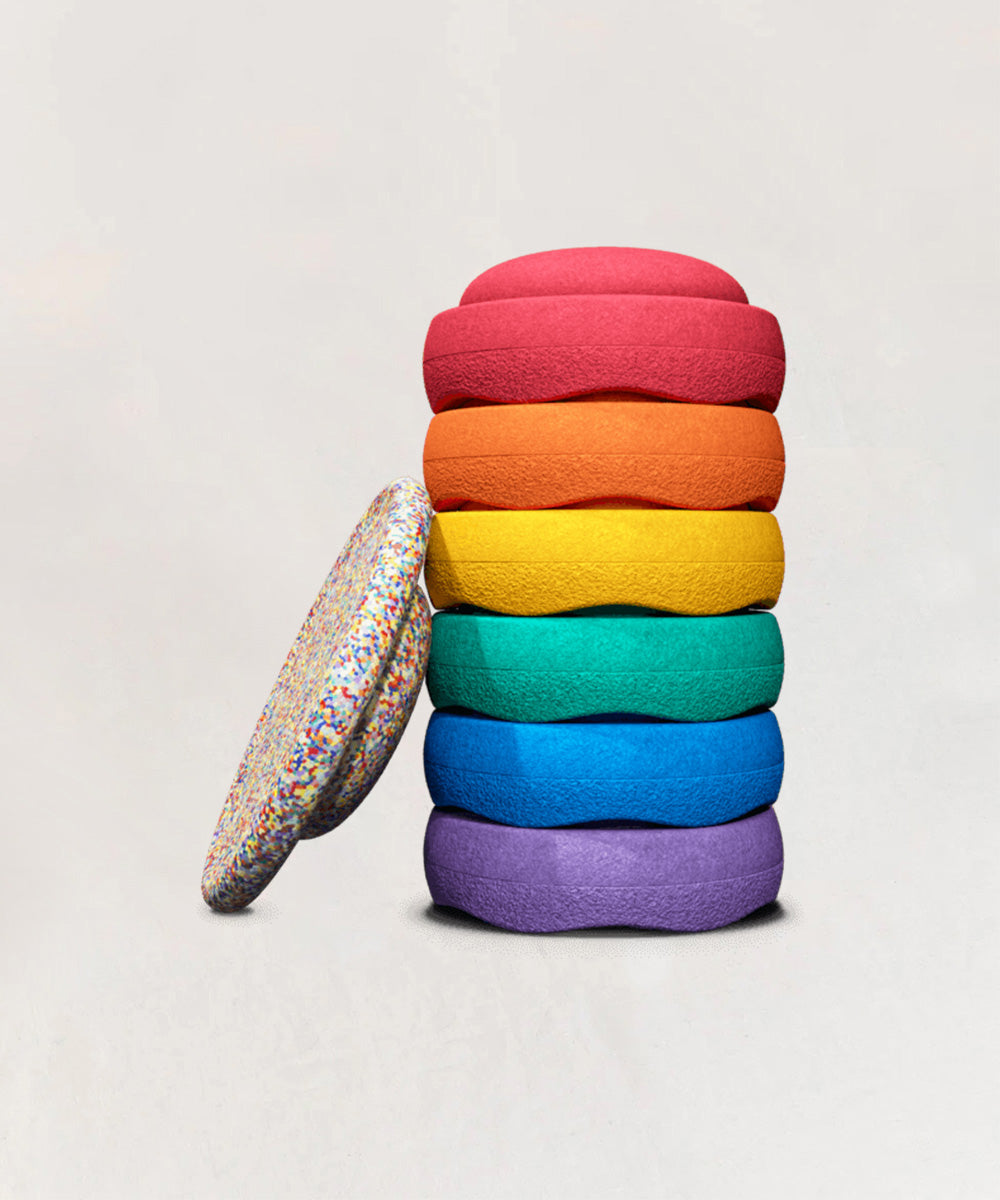 A stack of Le Stepping Stones - Rainbow Set cushions with a sprinkle-patterned cushion leaning against them.