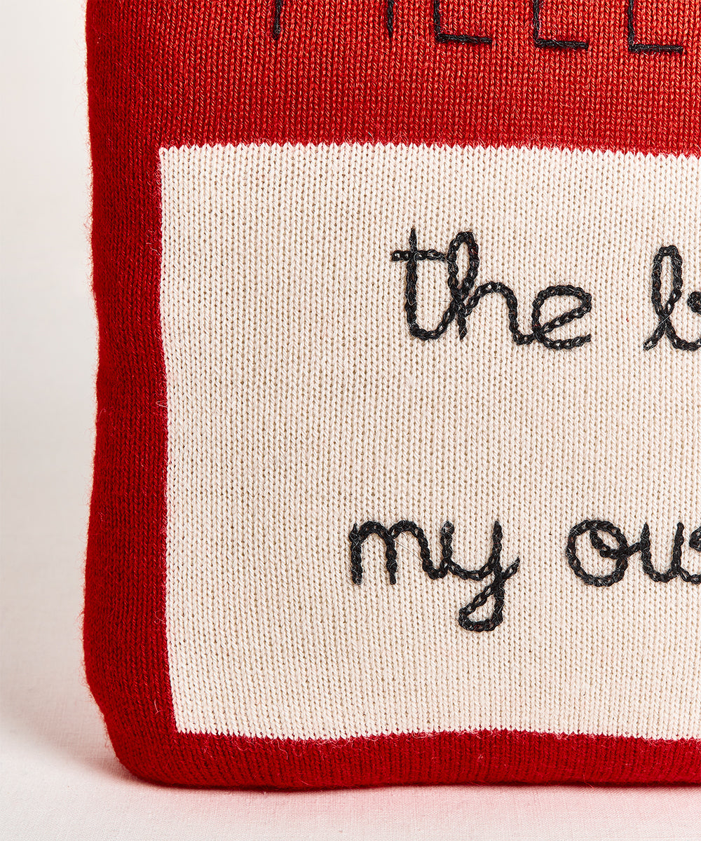A Name Tag Pillow in red and beige with "the best is yet to come" stitched in black cursive.
