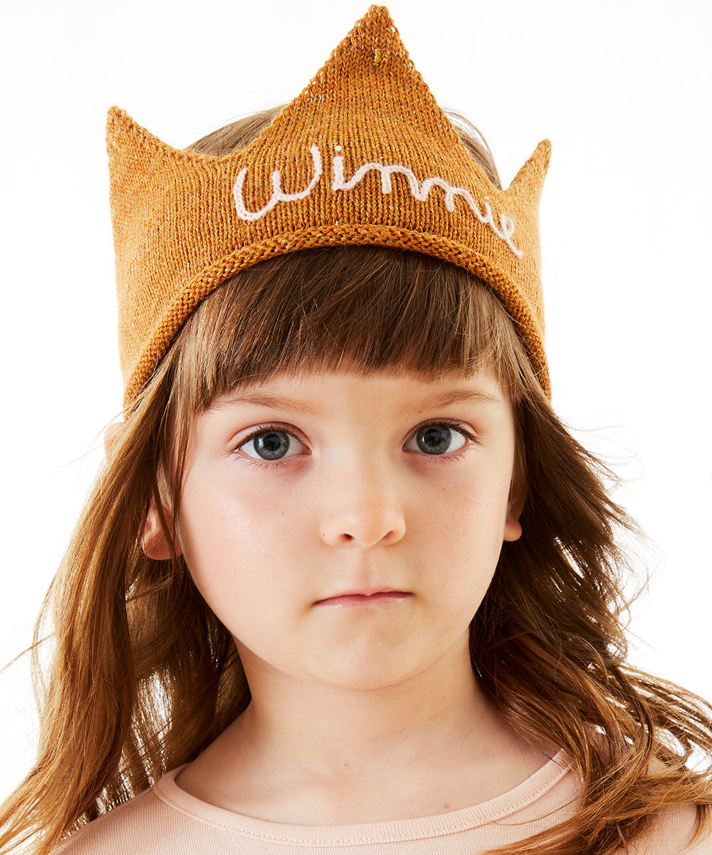 Young girl with brown hair wears a light pink Personalized Gold Crown headband, "Winnie" embroidered, looking at the camera.