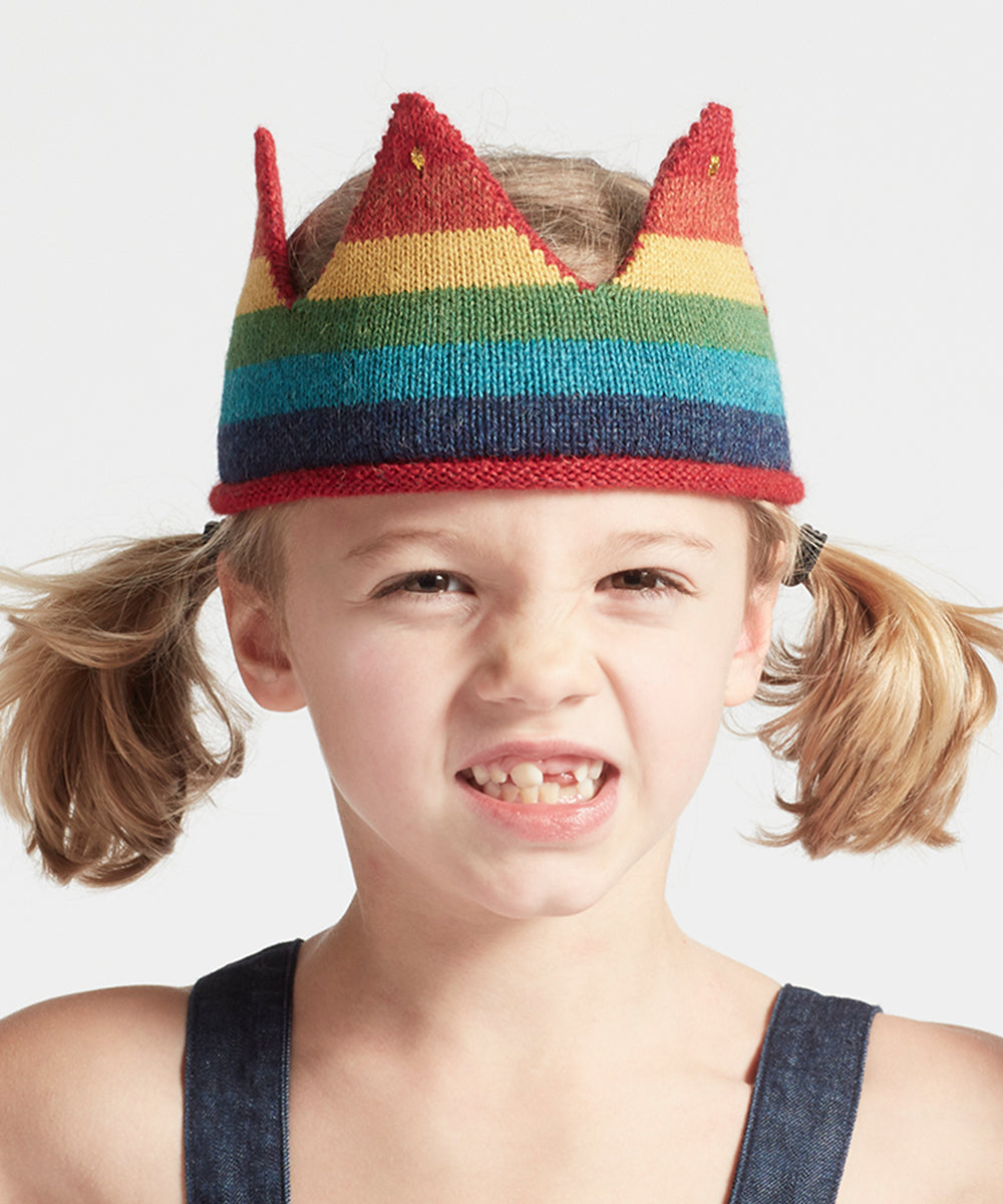 A young child with pigtails makes a playful face while wearing the Rainbow Crown.
