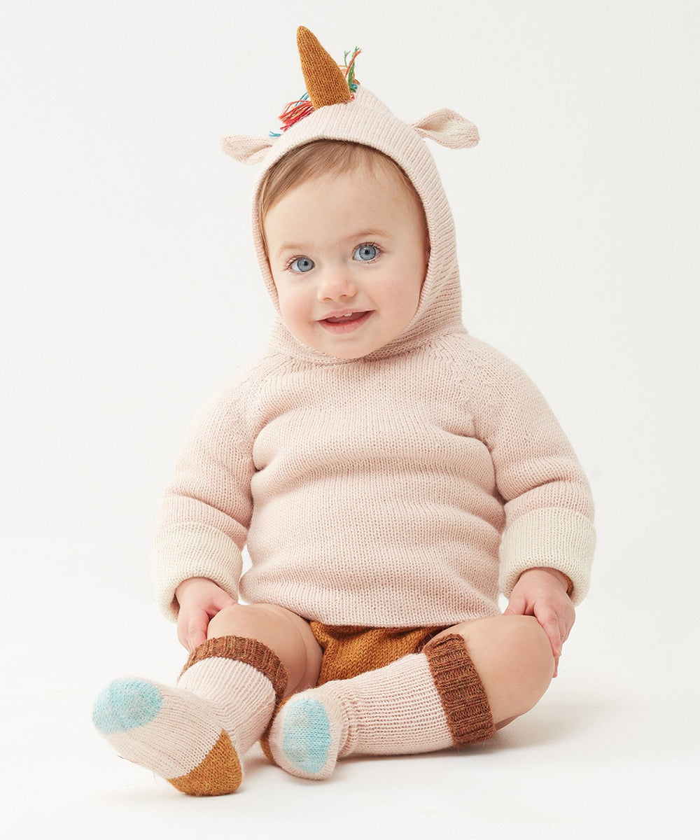 A baby wearing the Unicorn Hoodie sits on a white background, paired with wool shorts and matching socks.