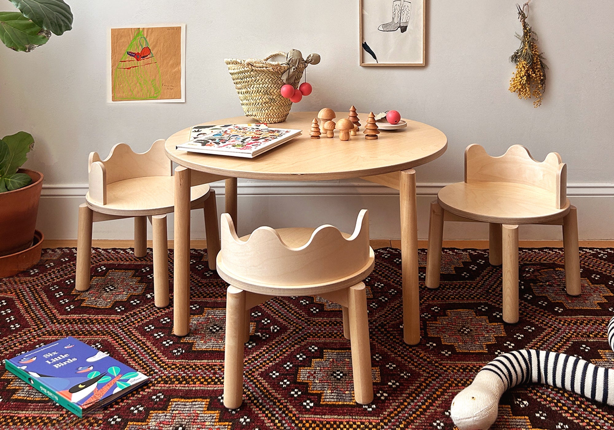 Children's wooden table and chairs set on a patterned rug, with art supplies and decor in a cozy room.