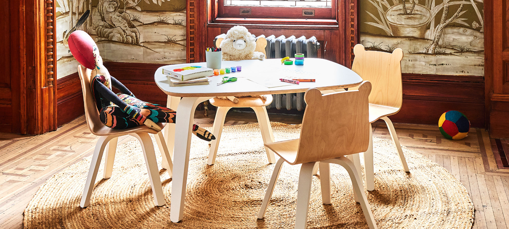 Child-sized table and chairs with plush toy and dinosaur figurine by a large window.