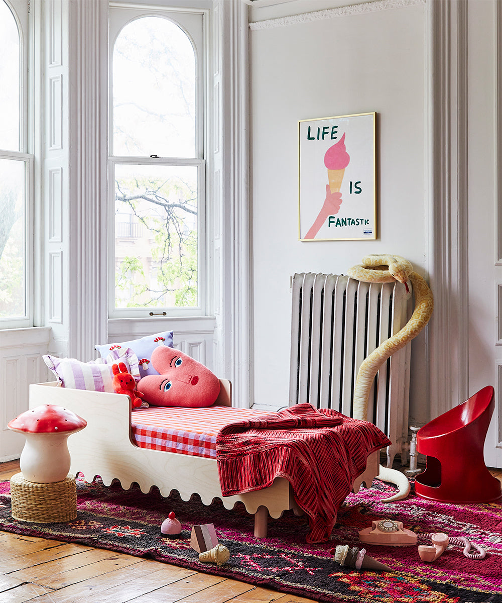 Children's bedroom featuring a small bed, stuffed toys, red decor, an art print on the wall, and the Le Big Mushroom Lamp by the window.