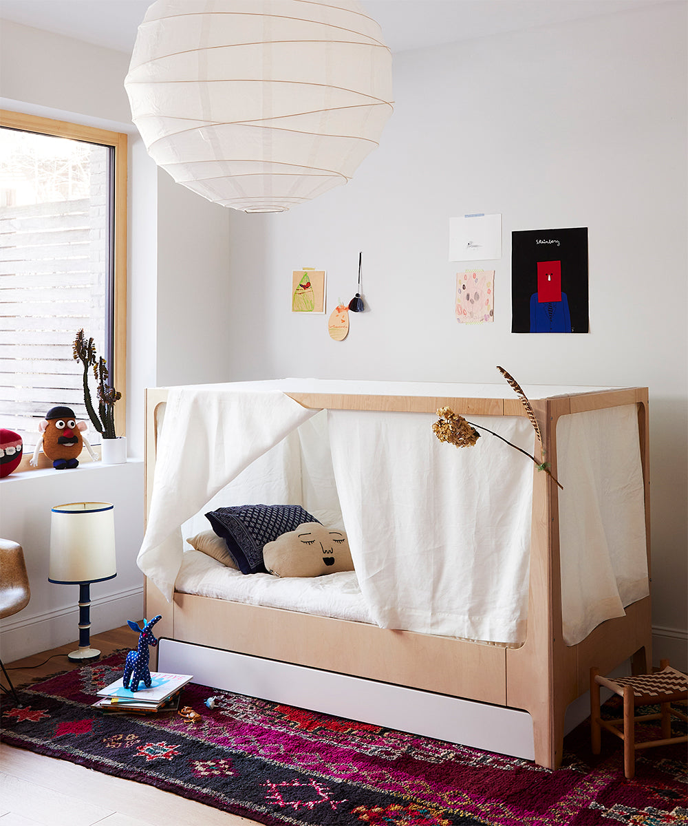 Childrens room featuring the Perch Nest Bed, a white canopy, a colorful rug, and decorative toys on a table and windowsill.