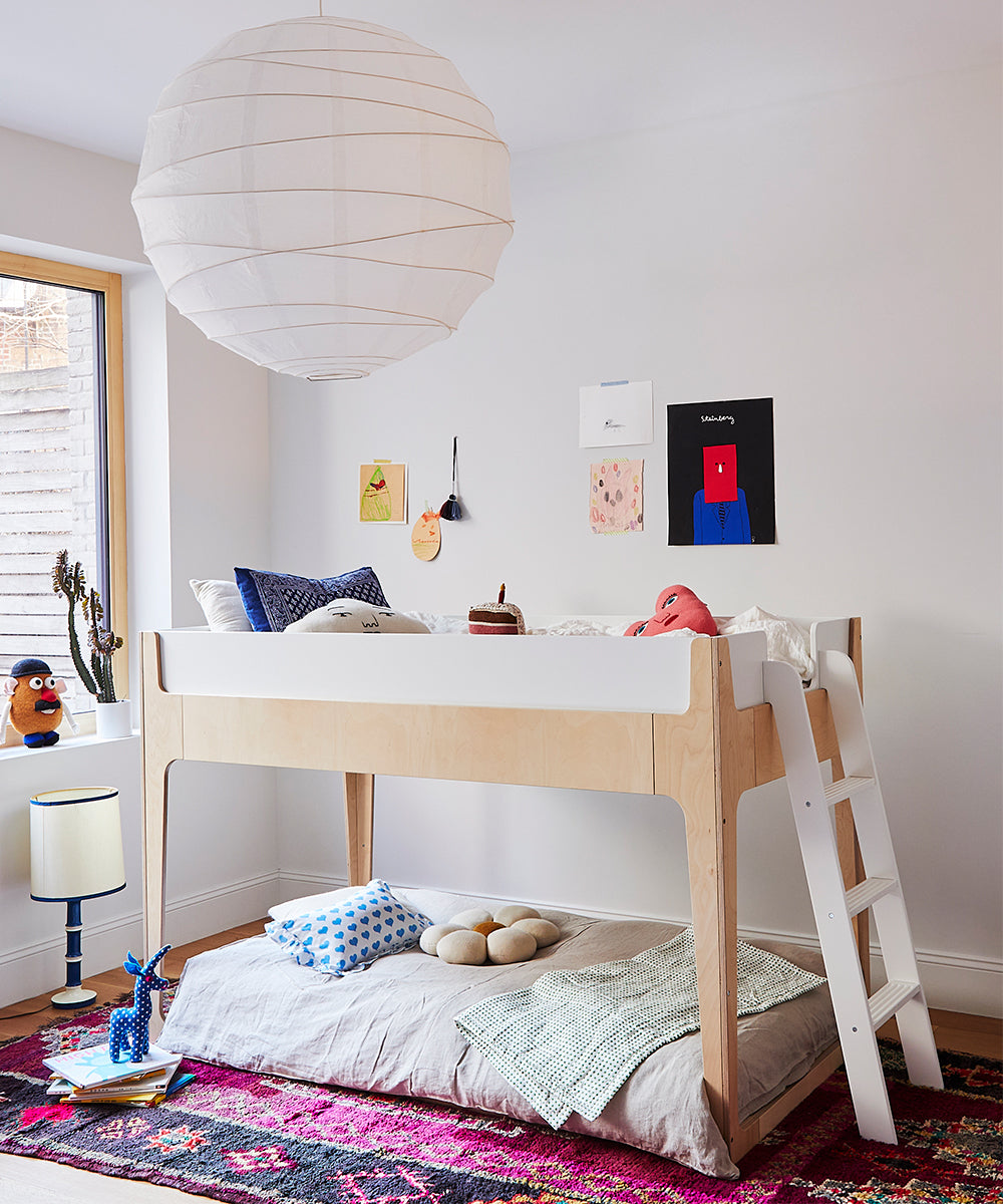 The cozy room features a Perch Nest Bed adorned with toys and cushions, complemented by a colorful rug and a large paper lantern.
