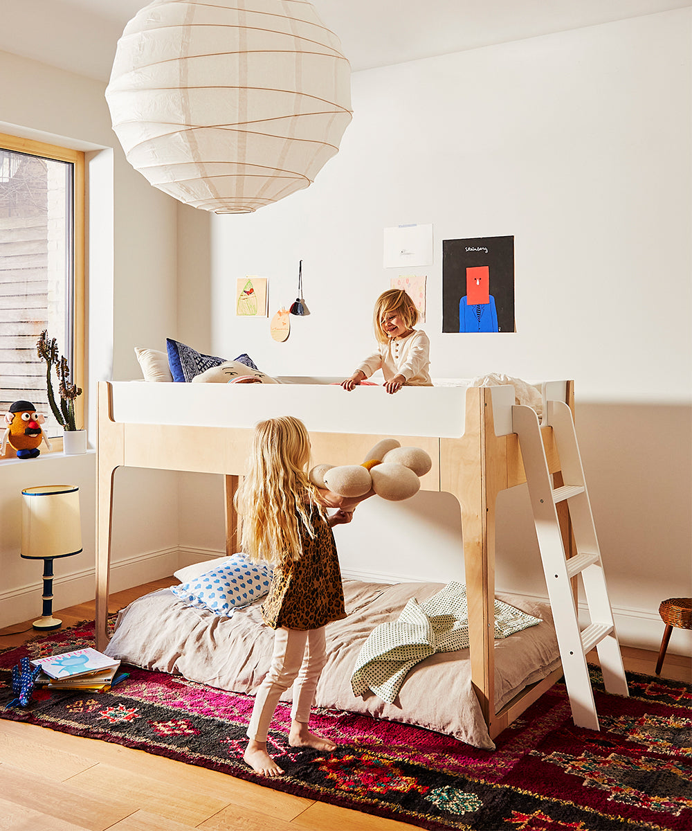 Two children play in a cozy room with the Perch Nest Bed and colorful decor, featuring a large paper lantern.